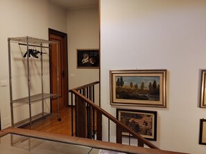 Una escalera con un estante metálico, barandilla de madera y obras enmarcadas en las paredes.