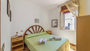 Een slaapkamer met een houten bed, een nachtkastje, een klein plankje en een raam met gordijnen.