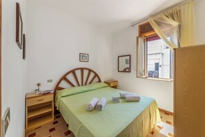 A bedroom with a wooden bed, a bedside table, a nightstand, a window with curtains, and a small shelf. - Leuca Relax & Sea n.5C, Castrignano del Capo, Italy (Castrignano del Capo)