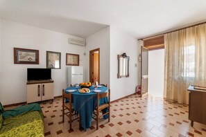 A dining area with a table set for two, a television on a cabinet, and a door leading to another room. - Leuca Relax & Sea n.5C, Castrignano del Capo, Italy (Castrignano del Capo)