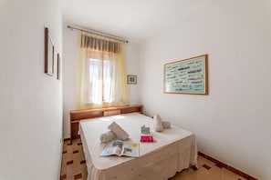 A hotel room with a bed, a bedside table, a window with curtains, a framed picture on the wall, and a small bedside table with a book and a red box. - Leuca Relax & Sea n.5C, Castrignano del Capo, Italy (Castrignano del Capo)