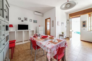 A dining area with a table set for four, a television, and a kitchen area with cabinets and a refrigerator. - Leuca Relax & Sea n.4C, Castrignano del Capo, Italy (Castrignano del Capo)