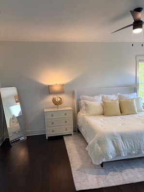 Ein Schlafzimmer mit einem Bett, einem Nachttisch, einer Lampe, einem Deckenventilator und einem Spiegel.