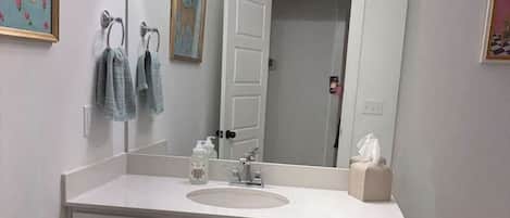 A bathroom with a white vanity, a large mirror, a toilet, and a black and white checkered rug.
