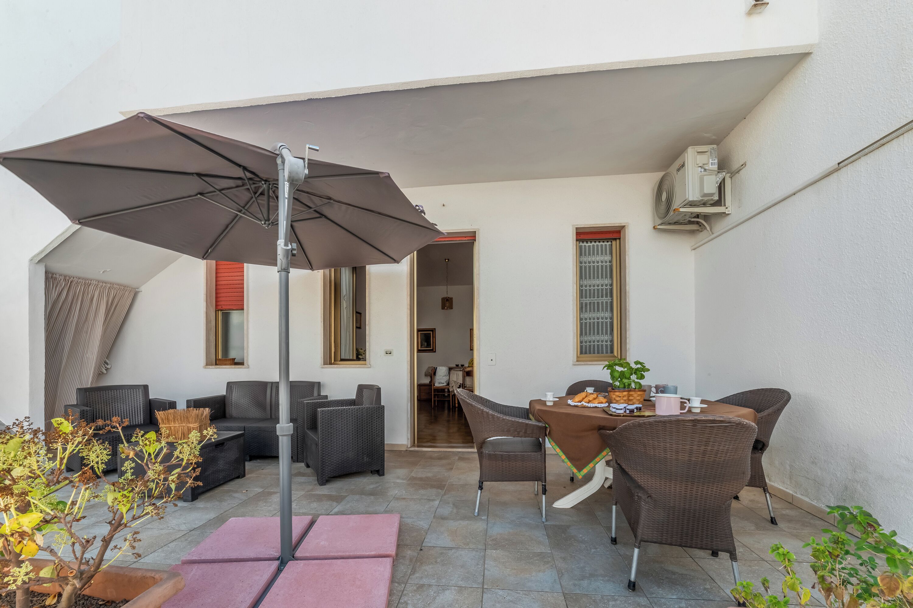 An outdoor patio area with wicker furniture, a table with a pink tablecloth, and a large umbrella.