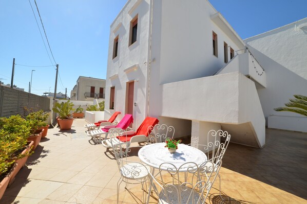 A white building with a patio area featuring a round table, white metal chairs, and potted plants. - Leuca Relax&Sea n.3C, Castrignano del Capo, Italy (Castrignano del Capo)