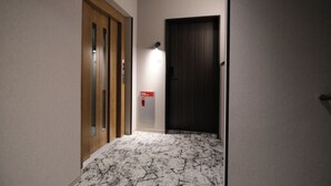 A hallway with a wooden door, a wall-mounted light, and a fire alarm. - Gran Marina (Osaka)