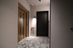 Un pasillo con una puerta de madera, una lámpara en la pared y un detector de incendios.