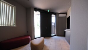 A hotel lobby with a red bench, a beige ottoman, a reception desk, and a large sliding glass door. - Gran Marina (Osaka)