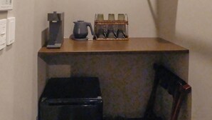 A small kitchenette with a coffee maker, a kettle, and a microwave. There is a trash bin and a chair in the corner. - Gran Marina (Osaka)