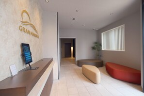 A reception area with a reception desk, a digital screen, a seating area, and a hallway leading to another room. - Gran Marina (Osaka shi minato ku chikko)