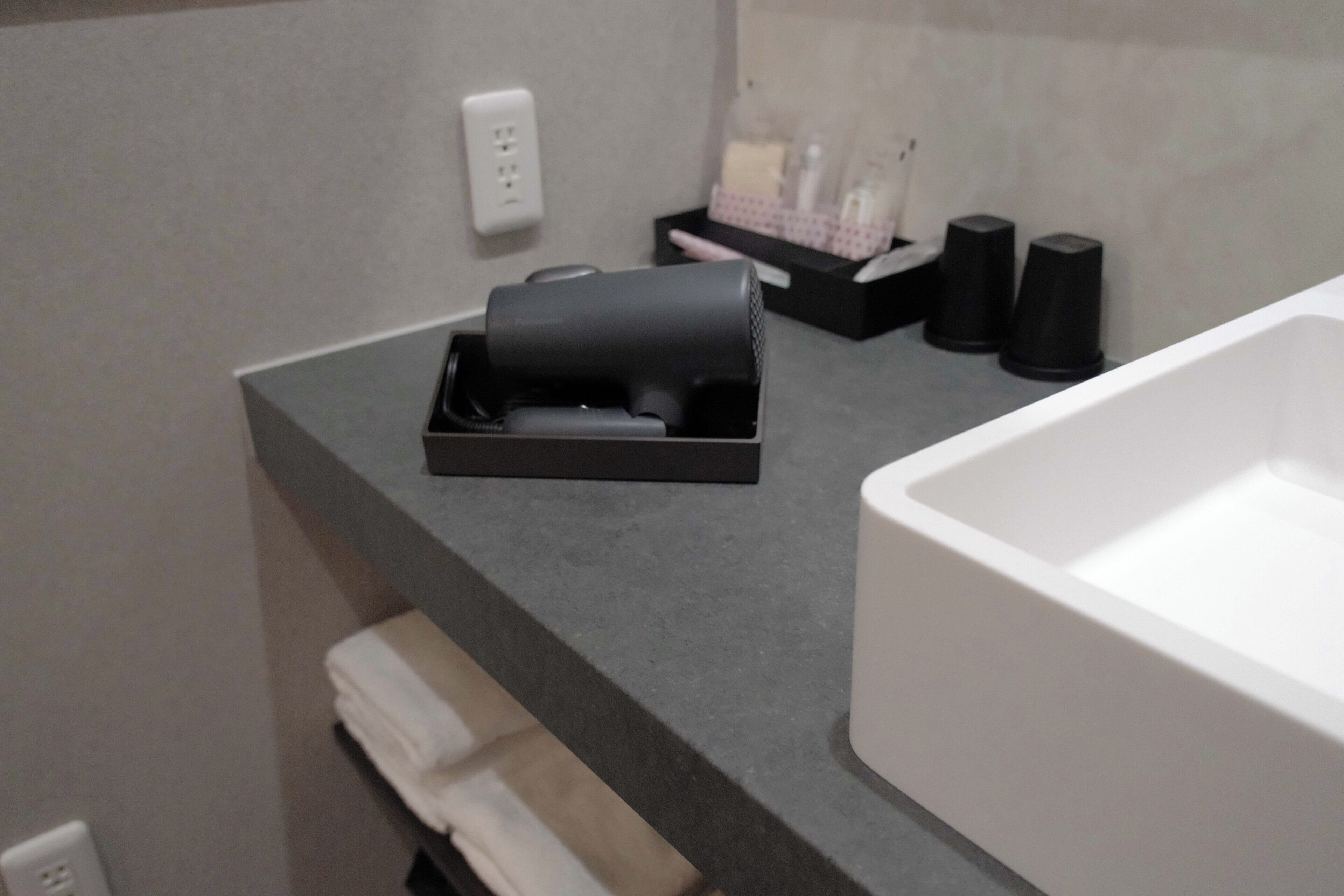 A bathroom with a white sink, a towel rack, a black soap dispenser, and a black container on the countertop.