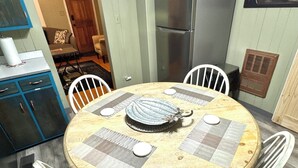 Une table de salle à manger ronde en bois, accompagnée de quatre chaises, d’un élément décoratif central et d’un buffet bleu avec des tiroirs.