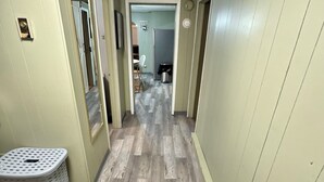 Un couloir avec un plancher en bois, un panier à linge et une porte donnant sur une pièce.