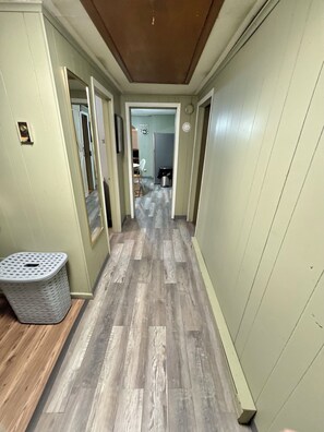 A hallway with wooden flooring, a laundry basket, and a door leading to a room. - ATV Trails and Skiing! Perfect 3-bedroom house in Rock (Rock)