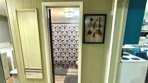Un couloir avec un mur orné d’un motif, une porte donnant sur une pièce et un coin cuisine équipé d’appareils électroménagers.