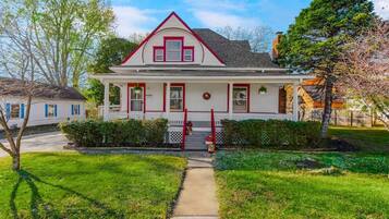 A two-story house with a front porch, a red door, and a small front yard.