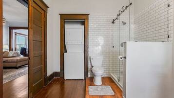 A compact bathroom with a toilet, a shower, and a washing machine.