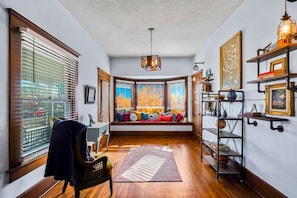 Une pièce chaleureuse avec un plancher en bois, un banc agrémenté de coussins colorés, un bureau avec une chaise et une bibliothèque.