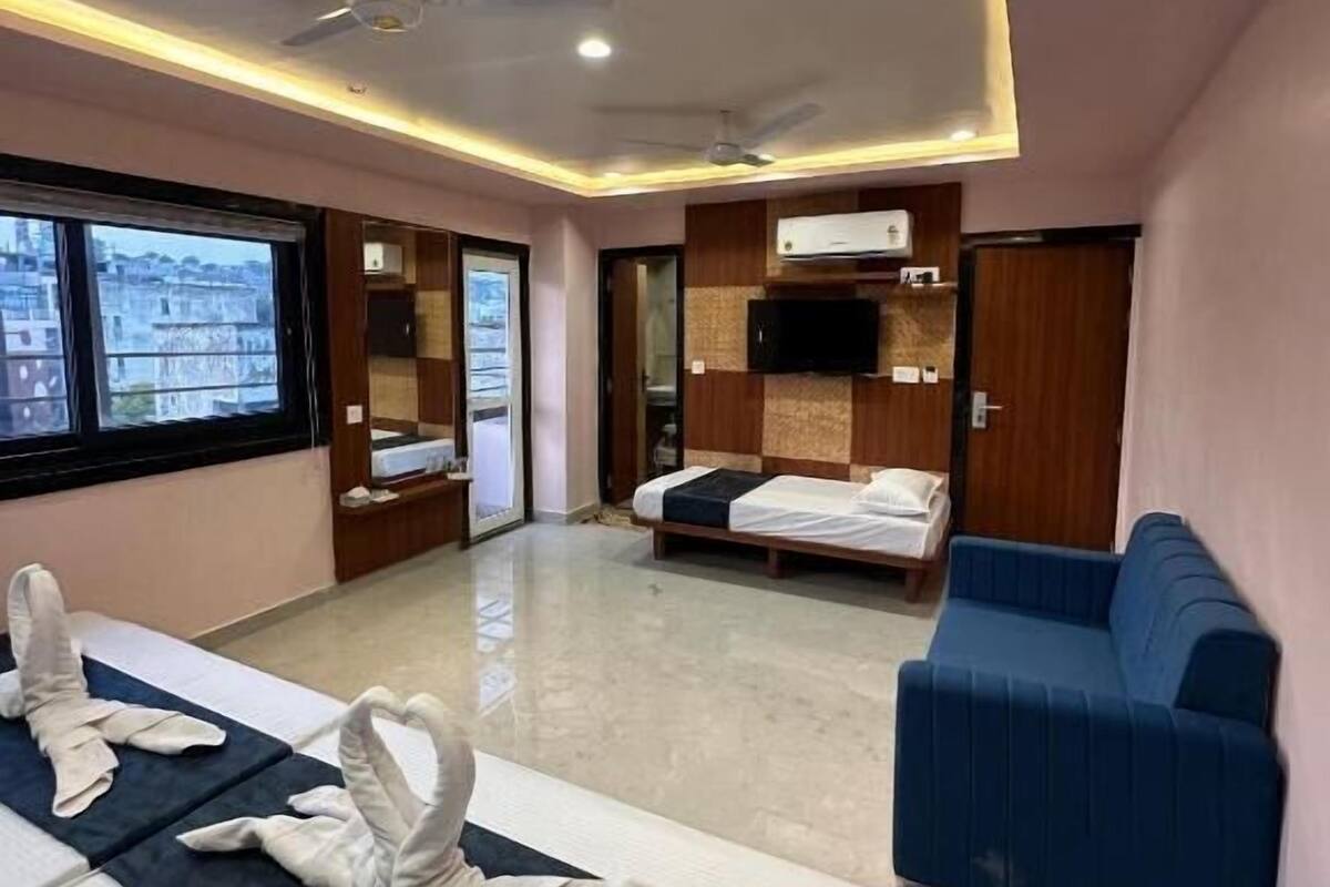 Habitación de hotel con cama, sofá azul, ventilador de techo y vistas por la ventana.
