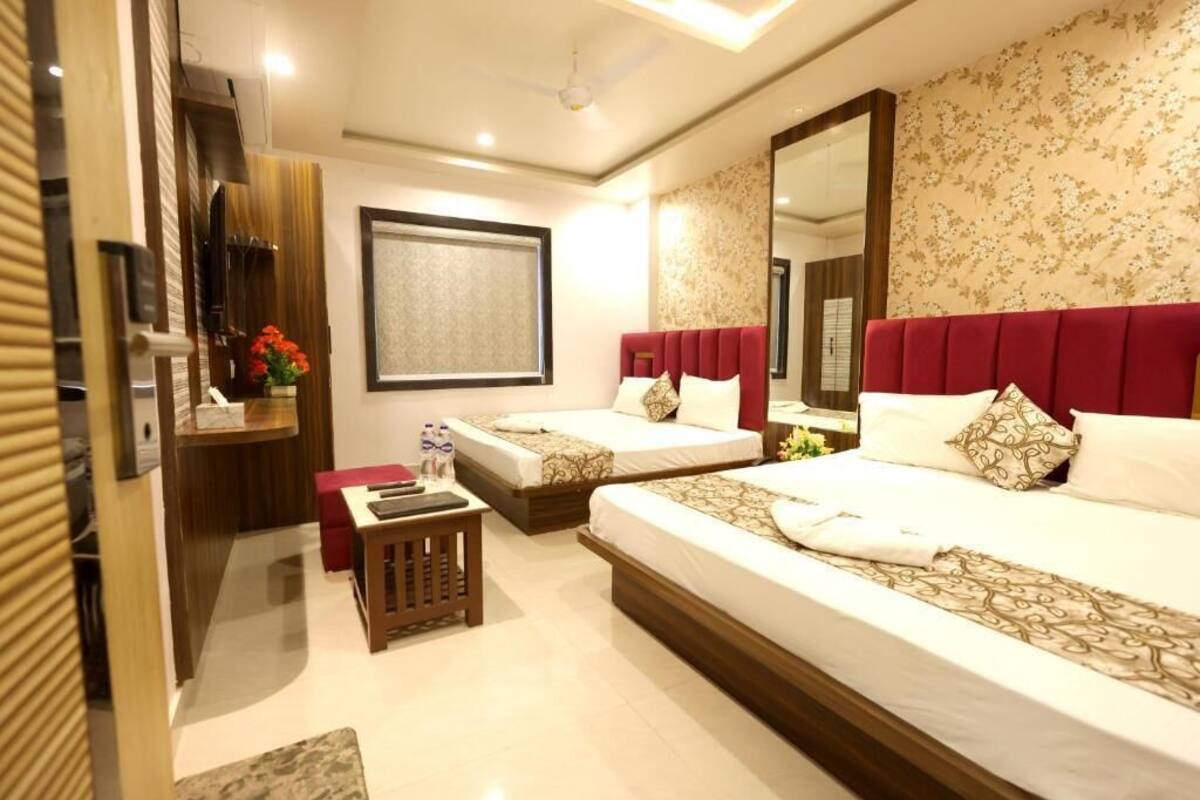 Una habitación de hotel con dos camas, un espejo grande, un armario de madera y una mesita con un jarrón de flores.
