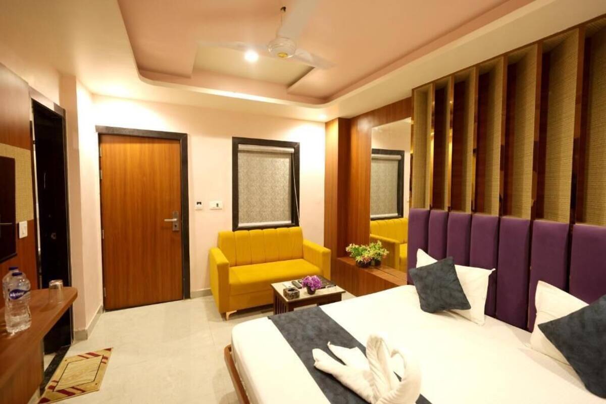 Una habitación de hotel con una cama, un sofá amarillo, una puerta de madera y un espejo.