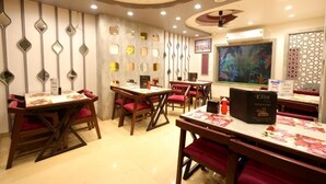 Un restaurant avec des tables en bois et des chaises à coussins rouges, un ventilateur de plafond et des panneaux décoratifs sur les murs.