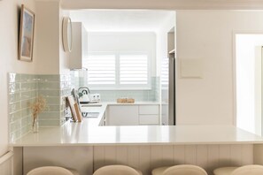 A modern kitchen with a white countertop, a toaster, and a window with blinds. - Hidden Sunshine Beach Gem • Steps to the Beach! (Sunshine Beach)