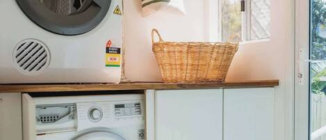 A laundry room with a front-loading washer and dryer, a wicker basket on the counter, and a window with a view of greenery.
