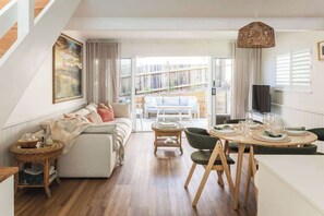 Una sala de estar moderna con un sofá, una mesa de comedor y sillas, una televisión y una escalera.