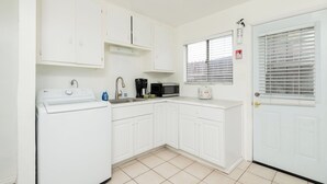 Une cuisine compacte avec des meubles blancs, un lave-linge, une machine à café et un four à micro-ondes.