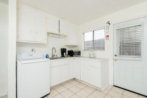 Una cocina compacta con armarios blancos, lavadora, cafetera y microondas.