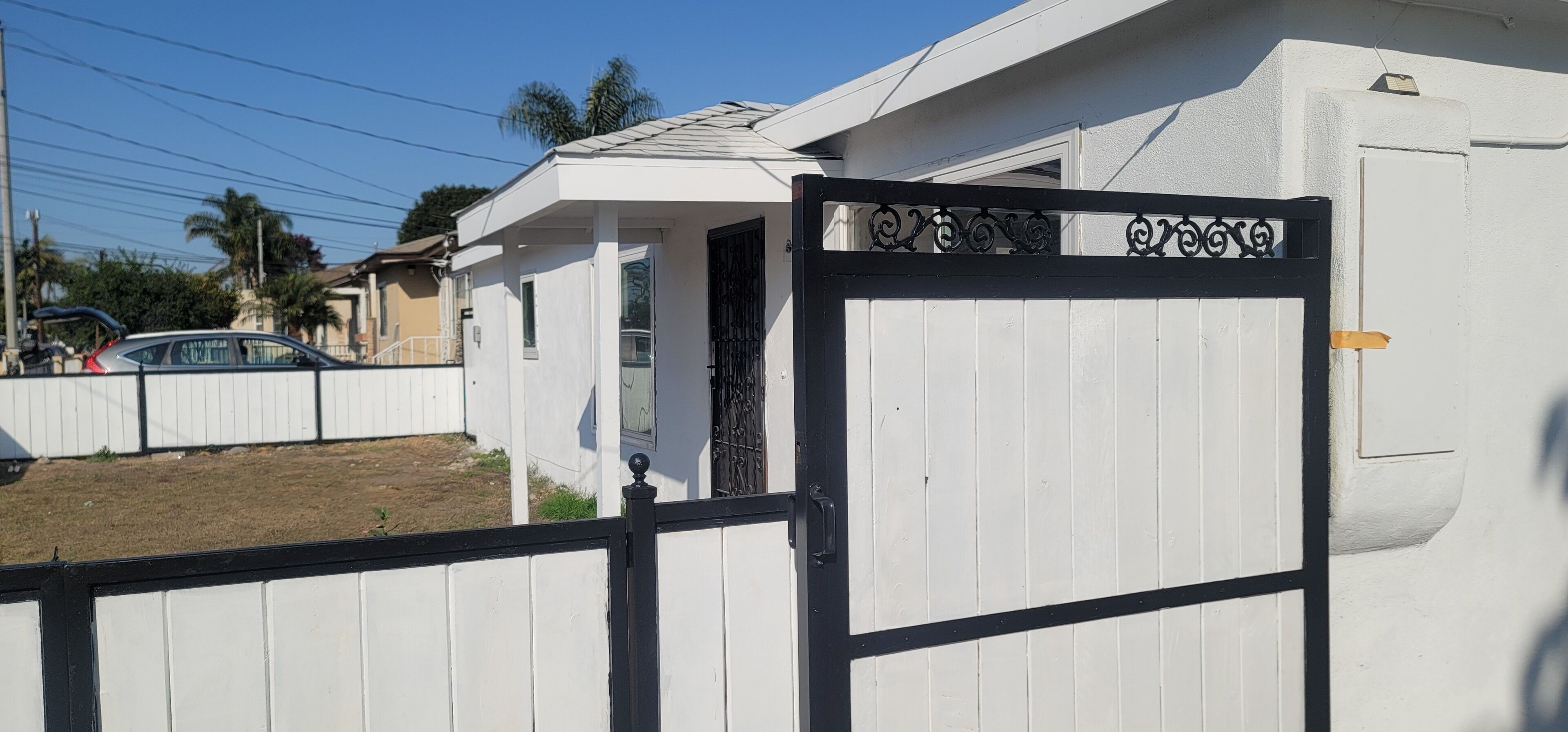Una entrada con portón a una propiedad de fachada blanca y portón negro.