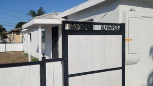 Une entrée fermée par un portail donnant accès à une propriété dont la façade est blanche et le portail noir.