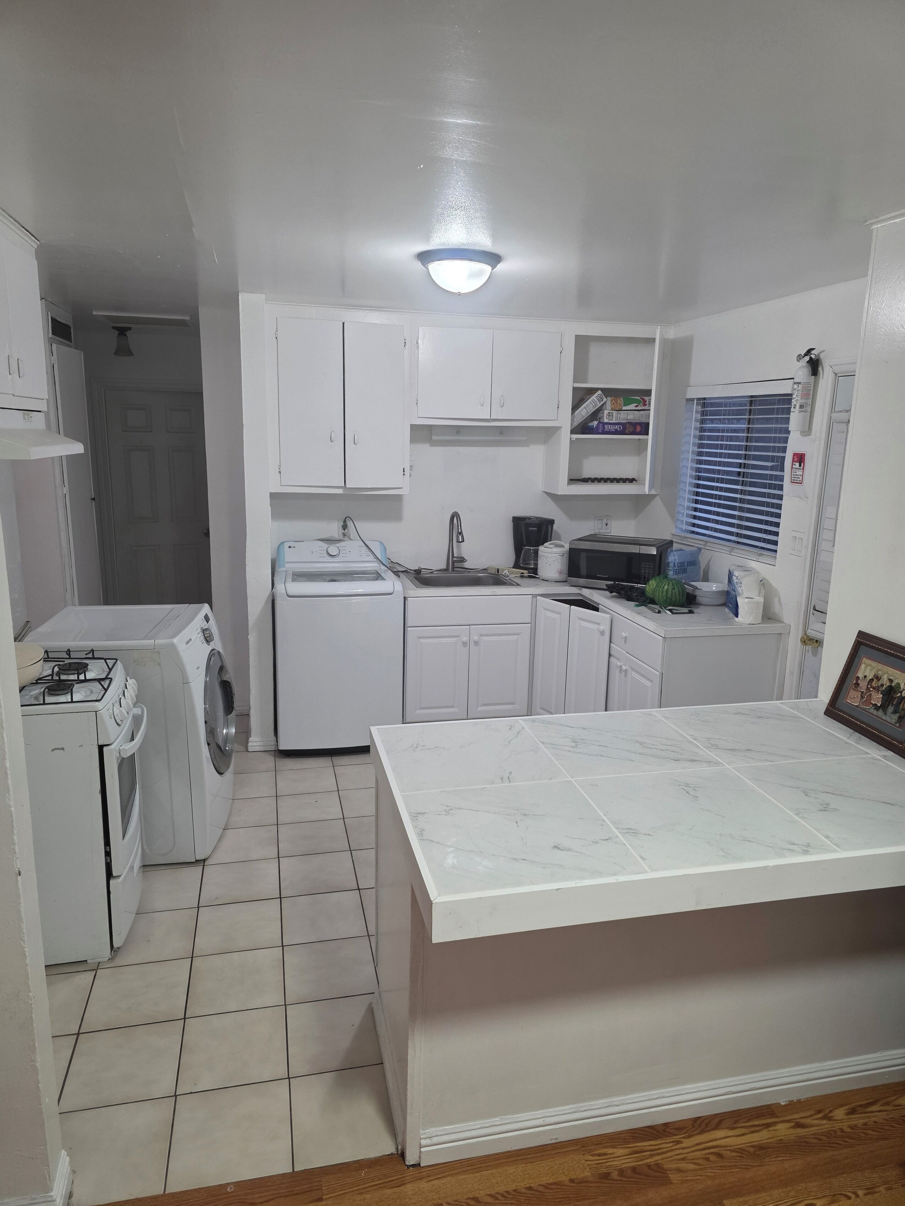 Una cocina compacta con muebles blancos, lavadora integrada, estufa a gas y piso de baldosas.