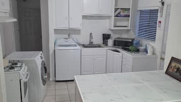 Una cocina compacta con muebles blancos, lavadora integrada, estufa a gas y piso de baldosas.