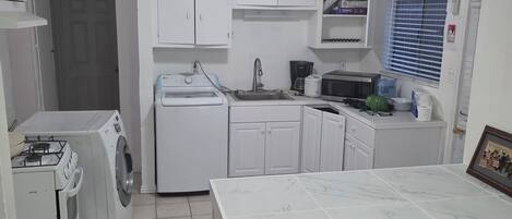 A compact kitchen with white cabinets, a built-in washing machine, a gas stove, and a tiled floor.