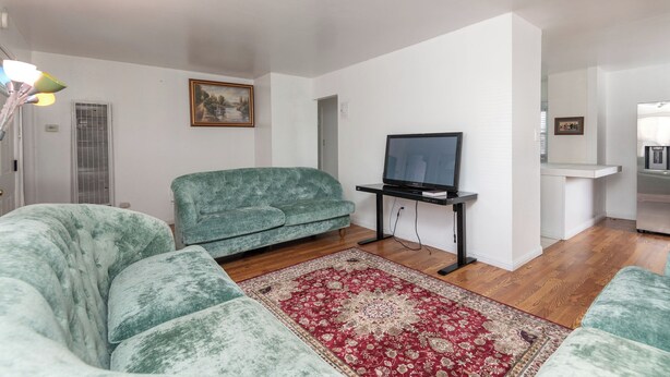 A living room with a sofa, a television on a stand, a patterned rug, and a painting on the wall.