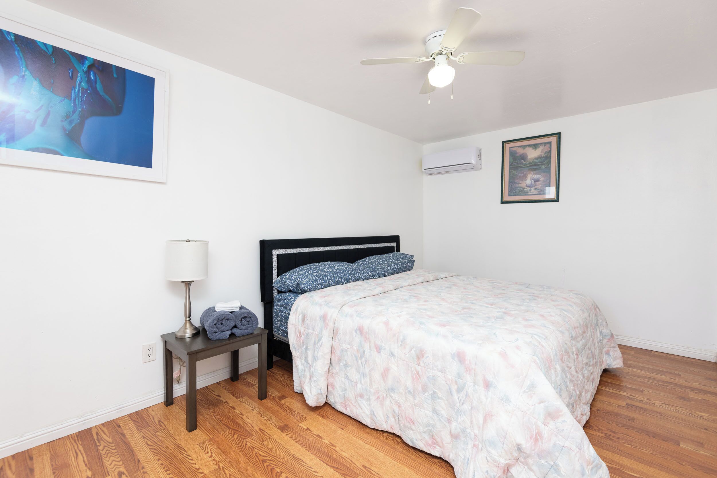 Un dormitorio con una cama, una mesita de noche, una lámpara, un aire acondicionado y un ventilador de techo.