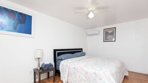 A bedroom with a bed, a nightstand, a lamp, an air conditioner, and a ceiling fan.