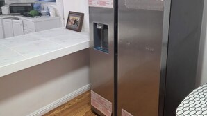 Une cuisine compacte dotée d’un plan de travail blanc, d’un four à micro-ondes, d’un distributeur d’eau et d’un réfrigérateur.