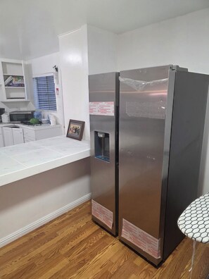 Cocina compacta con encimera blanca, microondas, dispensador de agua y refrigerador.