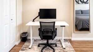 Una habitación con un escritorio blanco, una silla de oficina negra y un televisor montado.