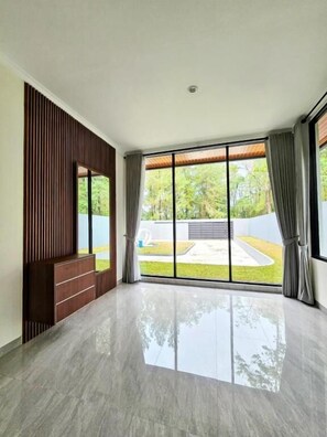 A spacious room with a large sliding glass door, a wooden panel wall, and a reflective floor.