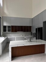 A modern kitchen with grey cabinets, a marble countertop, and a wooden accent.