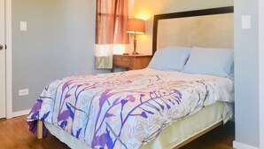 A bedroom with a bed, a nightstand, a lamp, and a window with curtains. - Spacious 3 bedroo, large livingroom and dining room. (Chicago)