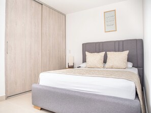 Ein Schlafzimmer mit Bett, grauem Kopfteil, zwei Kissen, einem Nachttisch und einem Holzschrank.