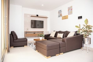Ein modernes Wohnzimmer mit Ecksofa, Couchtisch, Wand-Fernseher und einer Topfpflanze.