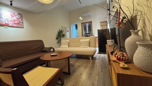 Un salon avec un canapé marron, une table basse ronde et un canapé beige. On y trouve des chaises en osier, un vase décoratif et un climatiseur fixé au mur.