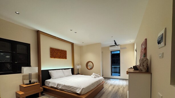 Une chambre moderne avec un grand lit, des tables de chevet, un miroir fixé au mur et une vue sur l’extérieur.